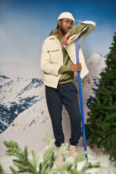 Schöner stylischer Mann in weißer Jacke und Mütze posiert mit Hockeyschläger, Winterkonzept — Stockfoto