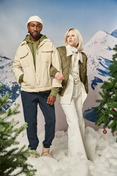 Красивая мультикультурная пара в теплой стильной одежде, позирующая рука об руку, зимняя концепция — стоковое фото