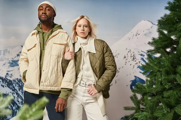 Elegante casal multicultural em roupa modish quente posando e olhando para a câmera, conceito de inverno — Fotografia de Stock