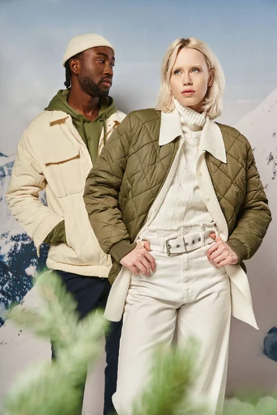 Atractiva pareja con estilo en ropa de abrigo posando junto a abeto con telón de fondo de montaña, invierno - foto de stock
