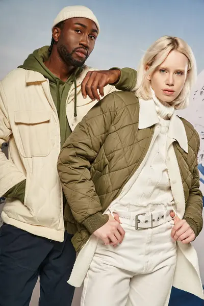 Elegante pareja joven en ropa caliente vibrante posando juntos y mirando a la cámara, concepto de invierno - foto de stock