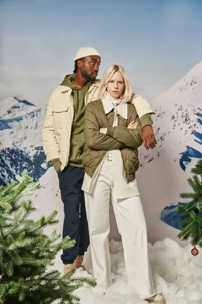 Beautiful voguish couple in warm winter jackets with mountain backdrop posing with arm on shoulder — Stock Photo