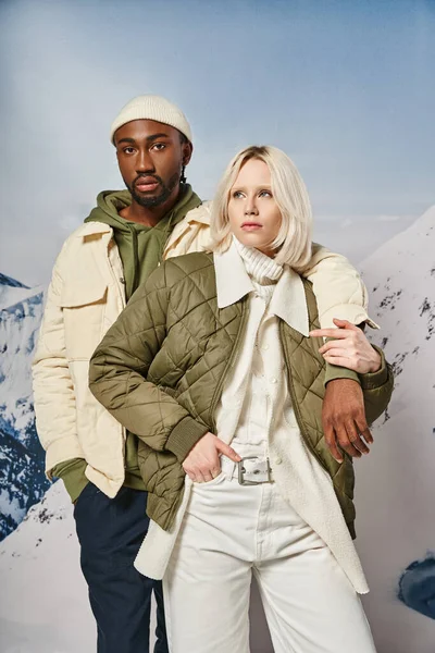 Atractiva pareja elegante en trajes de temporada posando junto con el telón de fondo de montaña, concepto de invierno - foto de stock