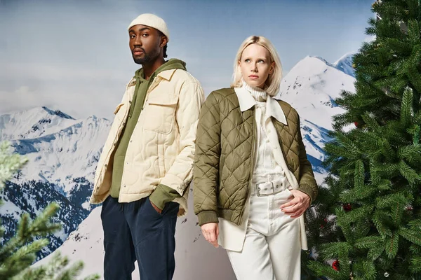 Beautiful stylish couple wearing warm modish jackets and posing next to fir trees, winter concept — Stock Photo