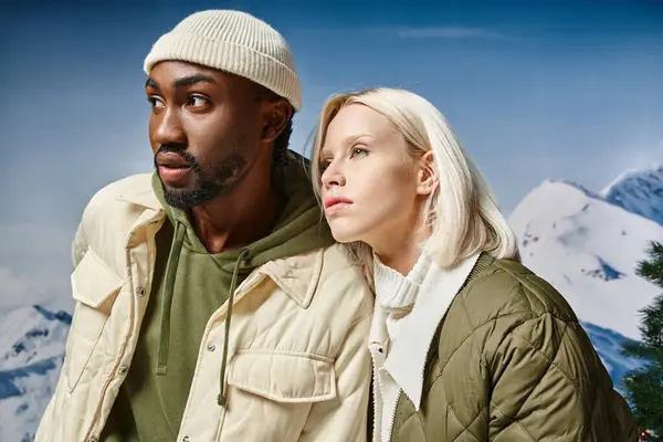 Atraente casal multirracial em casacos de inverno posando juntos e olhando para longe, estilo e moda — Fotografia de Stock