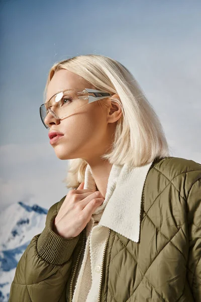 Mujer atractiva con elegante atuendo cálido con gafas y mirando hacia otro lado, mano sobre cuello, moda - foto de stock