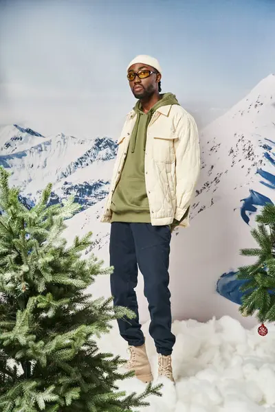Homem elegante na roupa quente elegante com chapéu gorro posando ao lado de pinheiros, conceito de inverno — Fotografia de Stock