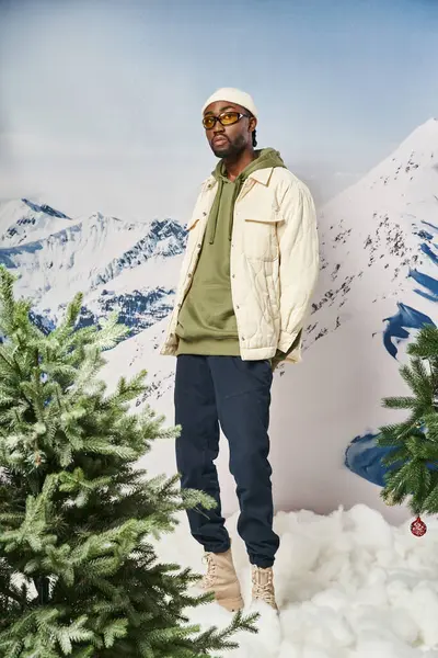 Homme à la mode dans une tenue chaude élégante avec chapeau de bonnet posant à côté de pins, concept d'hiver — Photo de stock