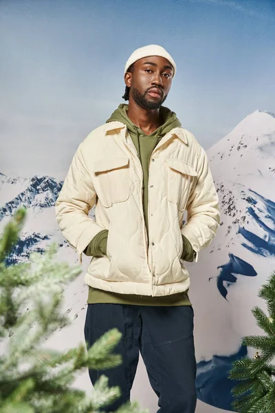Good looking man in white jacket and beanie hat posing with hands in pockets, fashion and style — Stock Photo