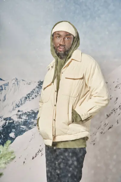 Élégant homme afro-américain posant avec les mains dans les poches debout sous la neige, concept d'hiver — Photo de stock
