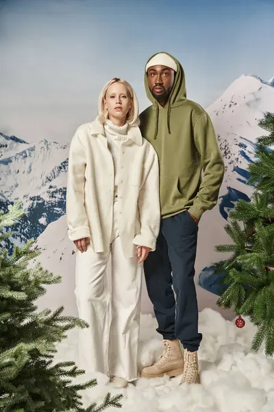 Beautiful multicultural couple standing side by side with mountain background, winter fashion — Stock Photo