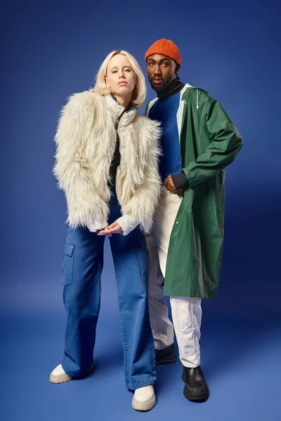 Modelos inter-raciais elegantes em trajes de inverno em pano de fundo azul, mulher loira e homem americano africano — Fotografia de Stock