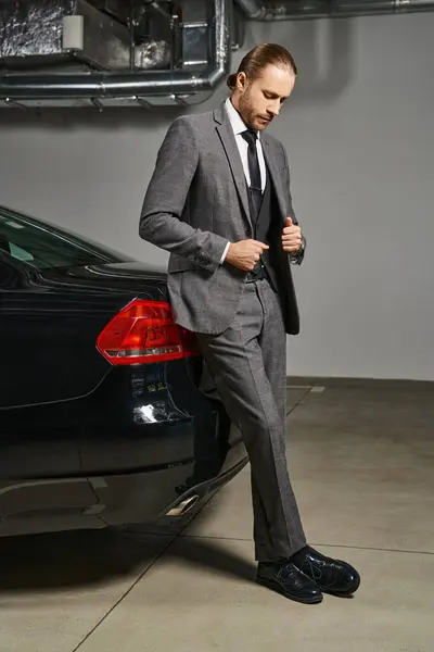 Homem bonito em terno elegante com gravata olhando para baixo no estacionamento perto de seu carro, conceito de negócio — Fotografia de Stock
