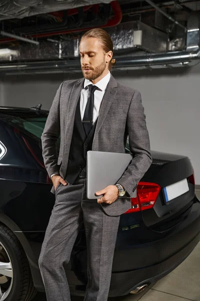 Bonito profissional em terno chique com gravata segurando laptop e posando na frente de seu carro, negócios — Fotografia de Stock