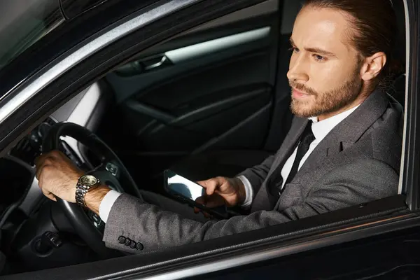 Homem elegante de boa aparência em terno chique atrás do volante com telefone nas mãos, conceito de negócio — Fotografia de Stock