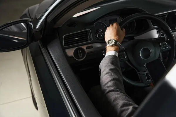 Vista ritagliata di elegante uomo d'affari con orologio da polso in tuta chic seduto dietro il volante — Foto stock