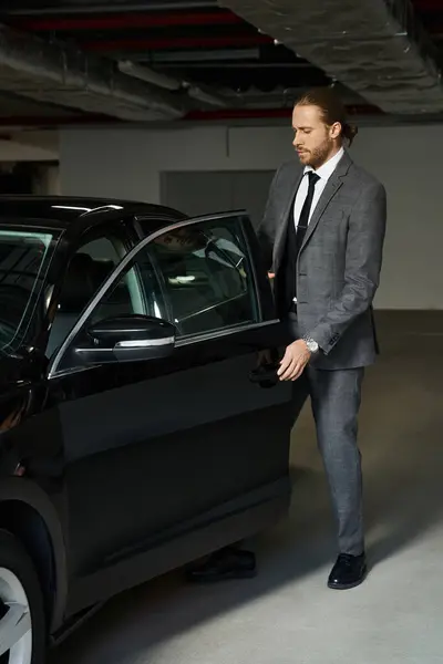 Attractive businessman with ponytail in smart elegant suit getting into his car on parking lot — Stock Photo