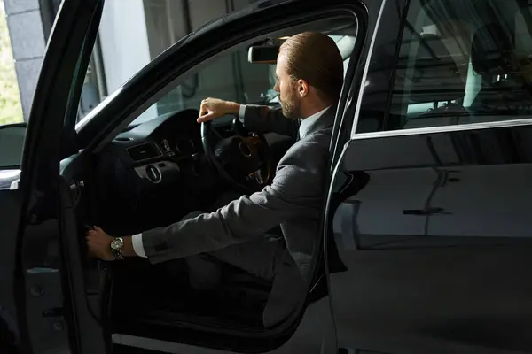 Bonito homem de negócios elegante com cabelo vermelho e rabo de cavalo em terno inteligente atrás do volante — Fotografia de Stock