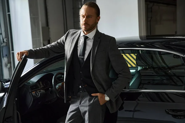 Homem barbudo atraente com estilo dapper posando perto de seu carro com mão no bolso, conceito de negócio — Fotografia de Stock