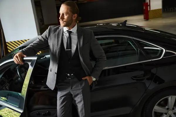 Привабливий витончений професіонал в шикарному розумному костюмі позує біля своєї машини з рукою в кишені, бізнес — стокове фото
