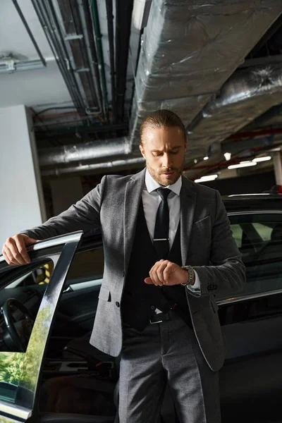 Handsome exquisite businessman with dapper style posing next to his car looking at his wristwatch — Stock Photo