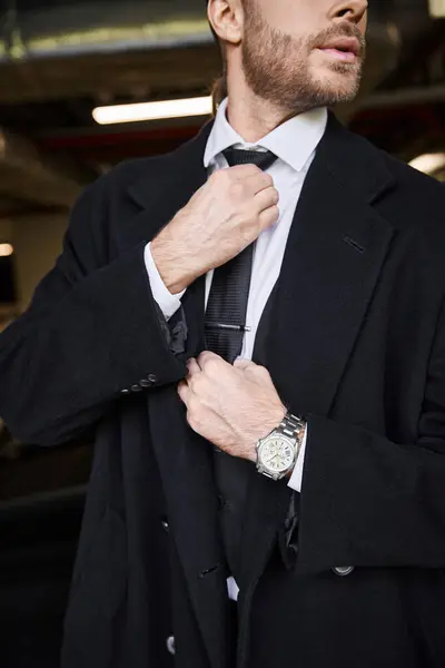 Cropped view of elegant businessman with beard in smart attire fixing his tie on parking lot — Stock Photo