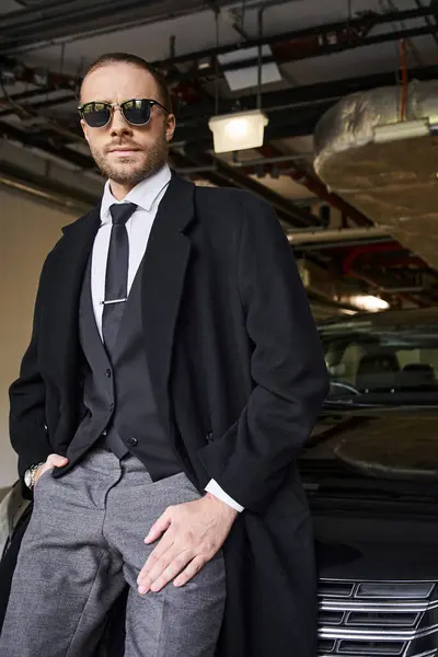 Apuesto hombre de negocios elegante con gafas de sol y corbata posando junto a su coche - foto de stock