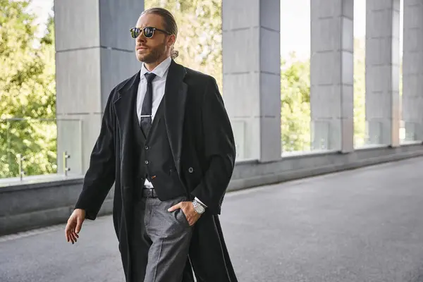 Homem elegante bonito em terno preto andando ao ar livre com a mão em seu bolso, conceito de negócio — Fotografia de Stock