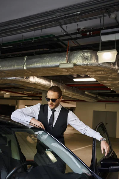 Attractive bearded man with red hair in black vest with sunglasses posing near his car, business — Stock Photo