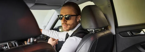 Appealing businessman with sunglasses looking at camera while behind steering wheel, banner — Stock Photo