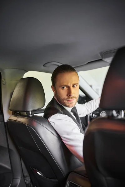 Atraente barbudo homem em colete preto olhando para trás, enquanto atrás volante, conceito de negócio — Fotografia de Stock