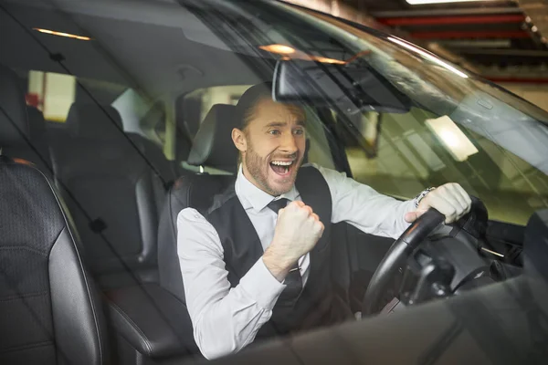 Joyous bearded professional in black vest cheering behind steering wheel, business concept — Stock Photo