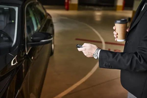 Vista ritagliata di uomo elegante in abito nero con tazza di caffè in mano utilizzando le chiavi della macchina, concetto di business — Foto stock
