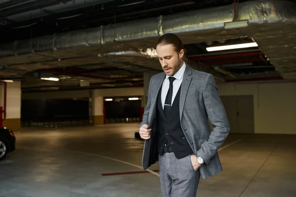 Handsome red haired man with tie and beard in gray suit posing on parking lot, business concept — Stock Photo