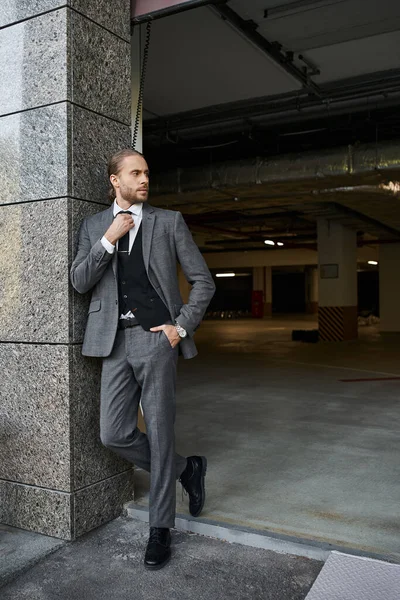 Appealing elegant man with beard in gray smart suit posing outside of parking lot, business concept — Stock Photo