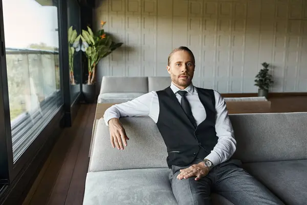 Schöner eleganter Mann in schwarzer smarter Weste sitzt auf dem Sofa und schaut in die Kamera, Geschäftskonzept — Stockfoto