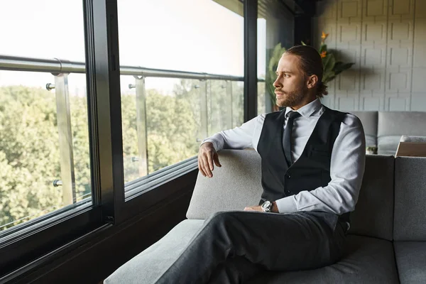 Schöner stilvoller Geschäftsmann in eleganter schicker Kleidung sitzt auf dem Sofa und schaut aus dem Fenster — Stockfoto
