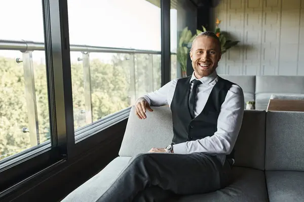 Cheerful handsome professional in business smart attire sitting on sofa and smiling at camera — Stock Photo