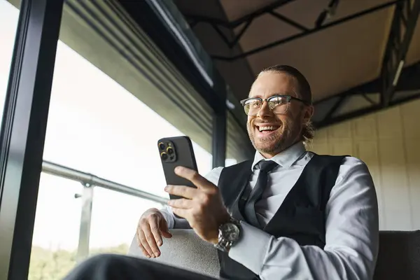 Fröhlich gut aussehender Mann in smarter Kleidung sitzt und schaut auf Handy, Geschäftskonzept — Stockfoto