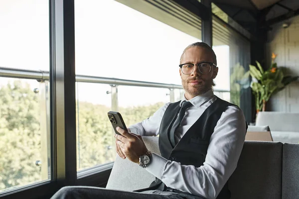 Attraente elegante uomo d'affari in abito intelligente con occhiali che tengono il telefono e guardando la fotocamera — Foto stock