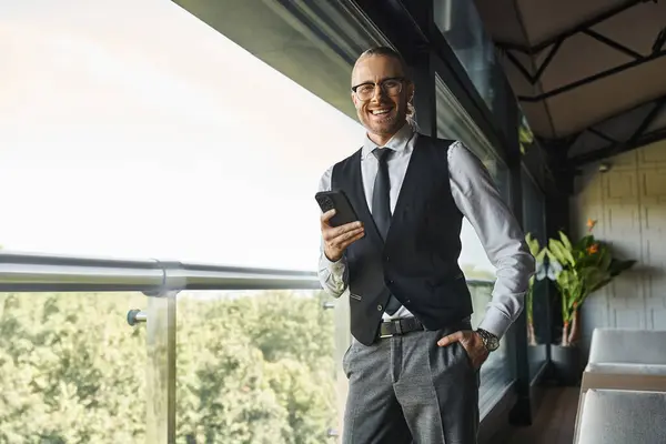 Cheerful handsome professional in smart attire with mobile phone smiling at camera, business concept — Stock Photo