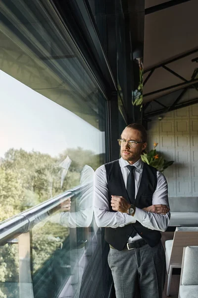 Schöner feiner Geschäftsmann in schicker schwarzer Weste mit Brille und Krawatte, der aus dem Fenster schaut — Stockfoto