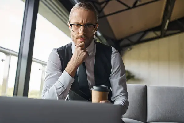 Nachdenklicher Mann in schicker Kleidung, der mit Kaffeetasse in der Hand an seinem Laptop arbeitet, Geschäftskonzept — Stockfoto