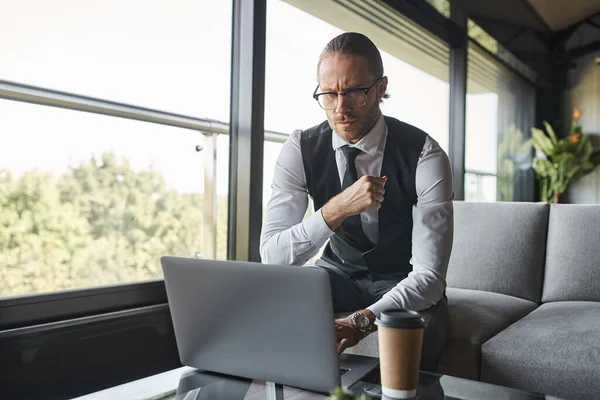 Nachdenklicher gutaussehender Mann, der aufmerksam an seinem Laptop arbeitet, Kaffeetasse auf dem Tisch, Geschäftskonzept — Stockfoto