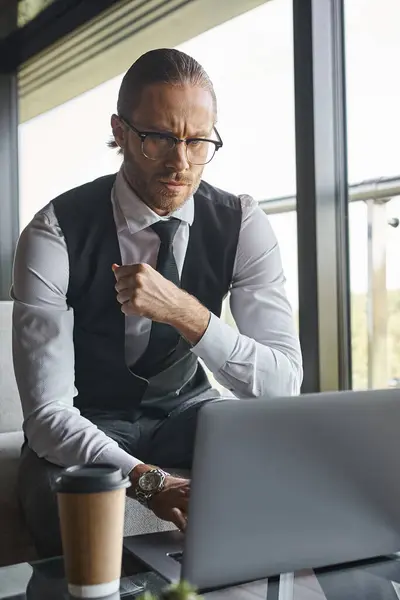 Vertical shot of thoughtful man with dapper style working hard with his laptop, coffee cup on table — Stock Photo