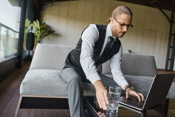 Bonito profissional em elegante traje inteligente trabalhando no laptop e pegar vidro de água, negócios — Fotografia de Stock
