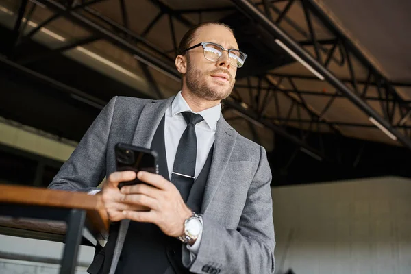 Atraente homem de negócios elegante com estilo dapper com óculos e gravata segurando telefone e olhando para longe — Fotografia de Stock