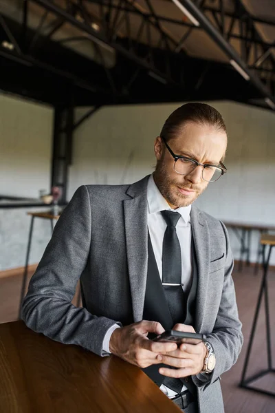 Profesional guapo pensativo con gafas en traje gris mirando a su teléfono móvil, negocio - foto de stock