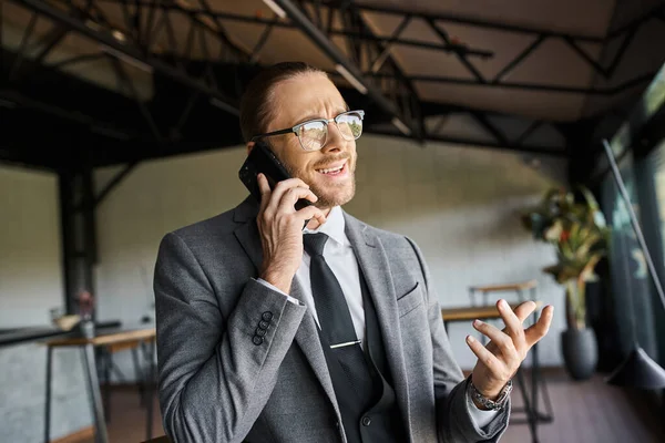 Confus beau homme d'affaires avec des lunettes en costume intelligent parler activement par téléphone mobile — Photo de stock