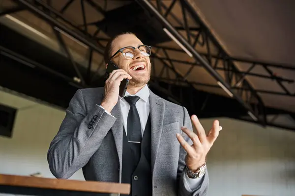 Gutaussehender, glücklicher Geschäftsmann im grauen eleganten Anzug, der munter telefoniert und aktiv gestikuliert — Stockfoto